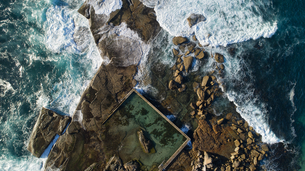 Aerial view of Newport Rock Pool with crashing waves against rugged coastal rocks and clear turquoise water in Sydney New South Wales Australia.