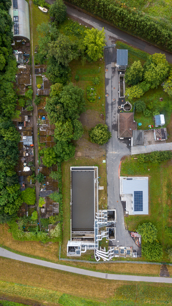 Aerial view of an industrial utility facility featuring a large rectangular tank complex piping systems and solar panels surrounded by lush green trees in Mannheim Germany.