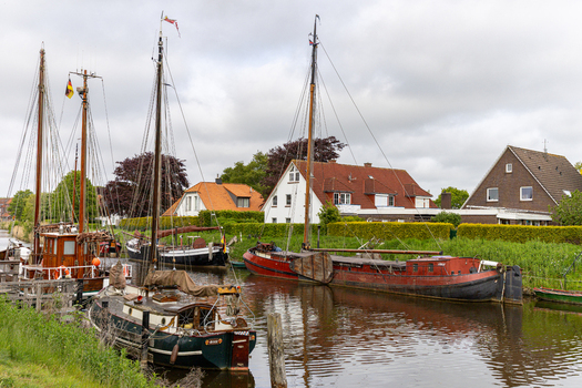 View of traditional sailing boats moored at Hafen Harlesiel with historic houses and green hedges under an overcast sky in Wittmund Lower Saxony Germany. View of traditional sailing boats moored at Hafen Harlesiel with historic houses and green hedges under an overcast sky in Wittmund Lower Saxony Germany.