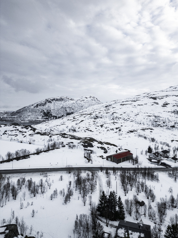 Aerial view of snow covered mountains and a winding road passing by small houses under a cloudy sky Ersfjord Troms Norway. Aerial view of snow covered mountains and a winding road passing by small houses under a cloudy sky Ersfjord Troms Norway.