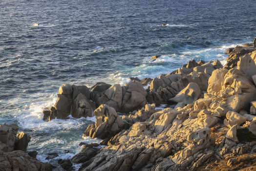 View of the granite rock formations at Capo Testa with waves crashing against the shore under warm golden hour light Capo Testa Sardegna Italy.