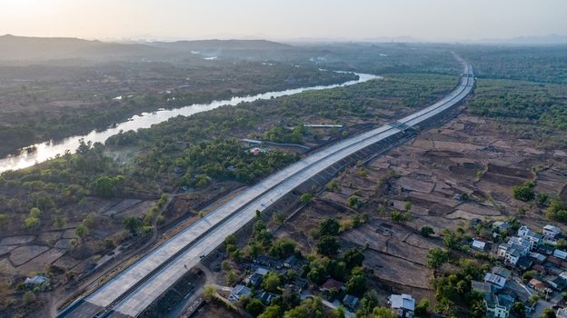 Aerial view of the JNPT highway featuring a long road winding through rural landscape with a river trees and residential buildings in Badlapur Maharashtra India. Aerial view of the JNPT highway featuring a long road winding through rural landscape with a river trees and residential buildings in Badlapur Maharashtra India.