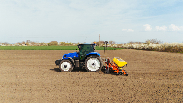 Aerial view of a blue tractor tilling the soil in a vast field under a pale sky Sremska Mitrovica Vojvodina Serbia. Aerial view of a blue tractor tilling the soil in a vast field under a pale sky Sremska Mitrovica Vojvodina Serbia.