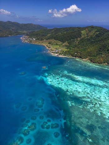 Aerial view of lush green hills and turquoise coral reefs along the coastline of Guanaja Bay Islands Department Honduras. Aerial view of lush green hills and turquoise coral reefs along the coastline of Guanaja Bay Islands Department Honduras.