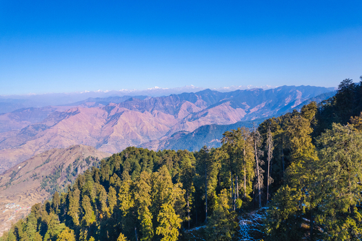 Aerial view of the lush green mountain ridges and dense coniferous forests under a clear blue sky in the Himalayan foothills Chakrata Uttarakhand India. Aerial view of the lush green mountain ridges and dense coniferous forests under a clear blue sky in the Himalayan foothills Chakrata Uttarakhand India.