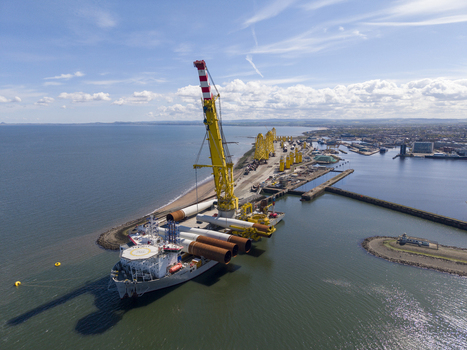 Edinburgh United Kingdom 06 May 2026 Aerial view of the dockside with a massive yellow crane loading wind turbine components onto a ship under a bright blue sky. Edinburgh United Kingdom 06 May 2026 Aerial view of the dockside with a massive yellow crane loading wind turbine components onto a ship under a bright blue sky.