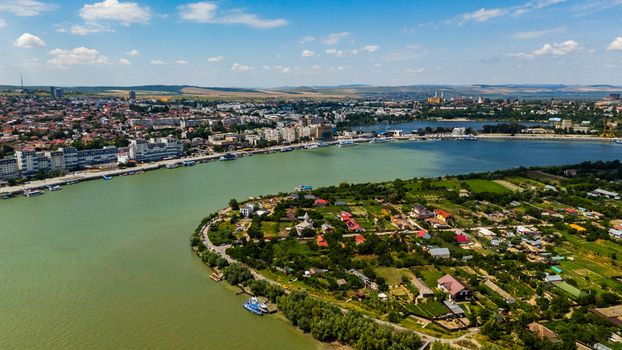 Aerial view of the city of Tulcea along the Danube River featuring urban buildings green gardens and boats on the water under a blue sky in Tulcea Tulcea Romania.