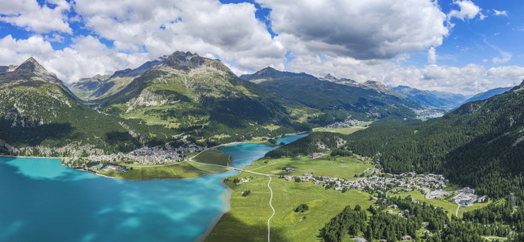 Aerial view of the village of Surlej and Lake Silvaplana surrounded by lush green meadows and towering mountains in Silvaplana Grisons Switzerland.