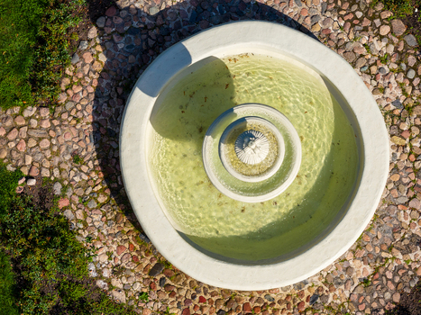 Aerial view of a circular stone fountain with clear water surrounded by a cobblestone path and green grass Taujenai Vilnius County Lithuania.
