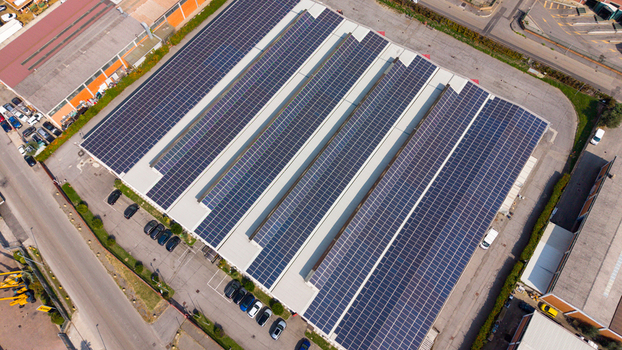 Aerial view of a transport company facility featuring extensive rooftop solar panels surrounding parking area with parked vehicles and industrial infrastructure in Milan Lombardy Italy.