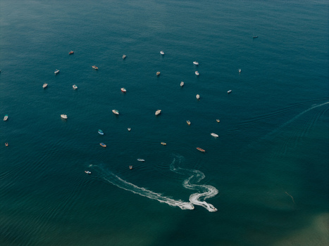 Aerial view of Baga Beach with numerous small boats anchored in the turquoise sea and jet skis leaving white wake trails on the water surface in Baga Goa India.