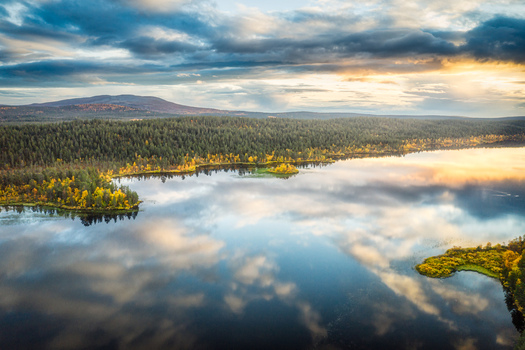 Aerial view of a serene lake reflecting dramatic clouds and golden hour light surrounded by dense pine forests and autumn foliage in Enontekio Lapland Finland. Aerial view of a serene lake reflecting dramatic clouds and golden hour light surrounded by dense pine forests and autumn foliage in Enontekio Lapland Finland.