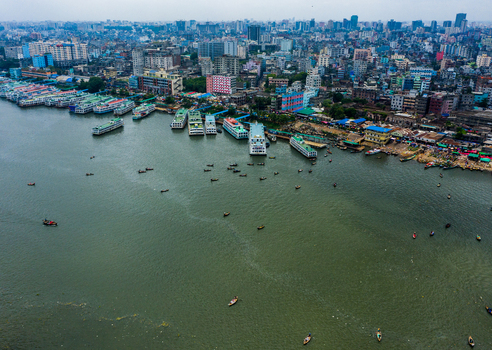 Aerial view of the Buriganga River with numerous passenger ferries and small boats docked along the busy riverbank set against the dense urban skyline of Dhaka Dhaka Division Bangladesh.