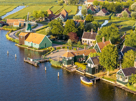 Aerial view of Zaanse Schans Windmill surrounded by traditional green wooden houses canals and lush green fields in Zaandam Noord Holland Netherlands.