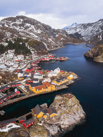 Aerial view of the quaint village with red roofed buildings clustered along the fjord s edge nestled between snow dusted mountains and the deep blue sea Nusfjord Nordland Norway.