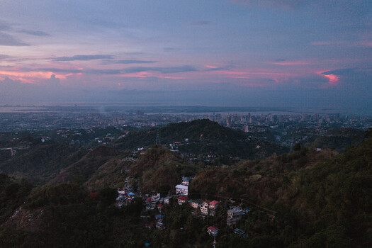 Aerial view of the lush Busay hills and residential houses overlooking the Cebu City skyline and the sea during a purple sunset in Cebu City Central Visayas Philippines.