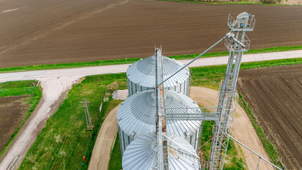Aerial view of silver grain silos gleaming under the open sky amidst a patchwork of green fields and bare earth Sremska Mitrovica Vojvodina Serbia. Aerial view of silver grain silos gleaming under the open sky amidst a patchwork of green fields and bare earth Sremska Mitrovica Vojvodina Serbia.