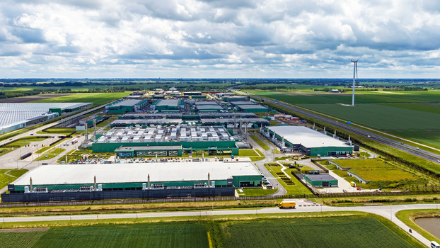 Aerial view of a large industrial data center complex with green rooftops a wind turbine and surrounding agricultural fields near a highway in Middenmeer North Holland Netherlands.