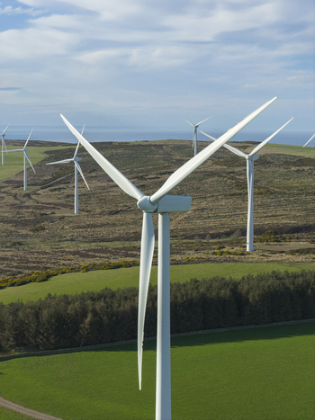 Aerial view of wind turbines of a windfarm standing over green fields and forests with the sea in the distance Scotland United Kingdom. Aerial view of wind turbines of a windfarm standing over green fields and forests with the sea in the distance Scotland United Kingdom.