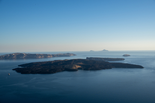 View of the volcanic islands of Nea Kameni and Palea Kameni in the Santorini caldera under a clear blue sky in Fira Greece. View of the volcanic islands of Nea Kameni and Palea Kameni in the Santorini caldera under a clear blue sky in Fira Greece.
