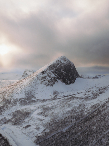 Aerial view of snow covered mountain peaks piercing the overcast sky a stark contrast against the white landscape Fjordgård Troms Norway. Aerial view of snow covered mountain peaks piercing the overcast sky a stark contrast against the white landscape Fjordgård Troms Norway.