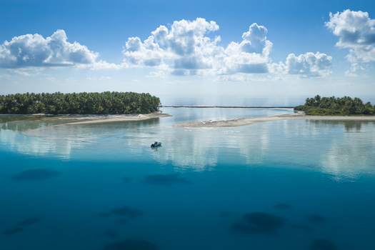 Aerial view of a small boat navigating the turquoise waters of a tropical island with lush palm trees under a bright blue sky in Kudahuvadhoo Dhaalu Atoll Maldives. Aerial view of a small boat navigating the turquoise waters of a tropical island with lush palm trees under a bright blue sky in Kudahuvadhoo Dhaalu Atoll Maldives.