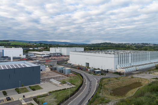 Aerial view of a large data center facility with multiple industrial buildings cooling systems and paved access roads in the United Kingdom.