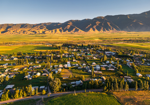 Aerial view of Chon Kemin valley featuring the village of Kaindy nestled among fields and rolling mountains under the warm glow of the golden hour in Kaindy Chuy Province Kyrgyzstan.