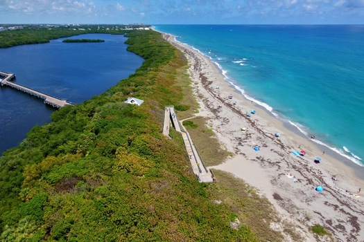 Aerial view of McArthur Beach featuring turquoise ocean waves a sandy shoreline with beachgoers and lush green coastal vegetation in North Palm Beach Florida United States.
