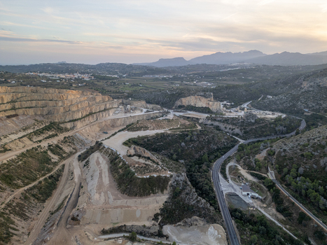 Aerial view of a large open pit quarry with terraced rock faces and winding roads set within the mountainous landscape of Teulada Valencian Community Spain.