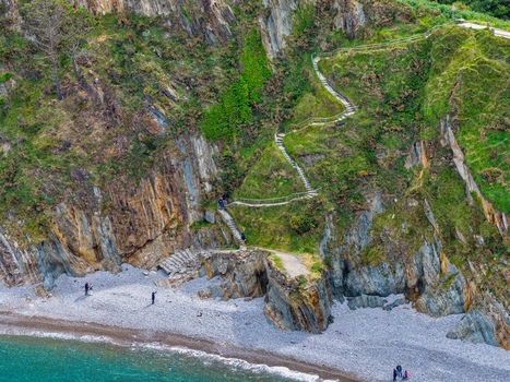 Aerial view of Silence Beach Viewpoint with a winding stone staircase on steep cliffs and people walking down to the pebble beach Cudillero Asturias Spain.