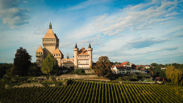 Aerial view of the medieval Vufflens le Chateau castle with its prominent square tower and turrets overlooking lush green vineyards under a blue sky in Vufflens le Chateau Vaud Switzerland. Aerial view of the medieval Vufflens le Chateau castle with its prominent square tower and turrets overlooking lush green vineyards under a blue sky in Vufflens le Chateau Vaud Switzerland.