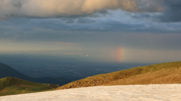 Aerial view of Le Colomby de Gex mountain ridge with snow patches a rainbow over the valley and dramatic storm clouds at sunset near Echenevex Auvergne Rhone Alpes France. Aerial view of Le Colomby de Gex mountain ridge with snow patches a rainbow over the valley and dramatic storm clouds at sunset near Echenevex Auvergne Rhone Alpes France.