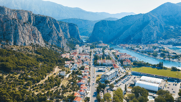 Aerial view of the town of Omis nestled between dramatic limestone cliffs and the Cetina River featuring red tiled rooftops and urban infrastructure in Omis Split Dalmatia County Croatia. Aerial view of the town of Omis nestled between dramatic limestone cliffs and the Cetina River featuring red tiled rooftops and urban infrastructure in Omis Split Dalmatia County Croatia.