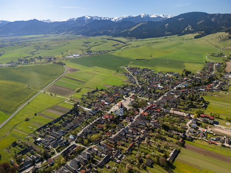 Aerial view of the historic village with its church tower surrounded by green fields and snow capped mountains in the distance Partizanska Lupca Zilina Region Slovakia.