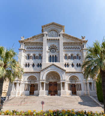 View of Saint Nicholas Cathedral with its ornate white stone facade Romanesque Byzantine architecture and palm trees under a clear blue sky in Monaco City Monaco. View of Saint Nicholas Cathedral with its ornate white stone facade Romanesque Byzantine architecture and palm trees under a clear blue sky in Monaco City Monaco.