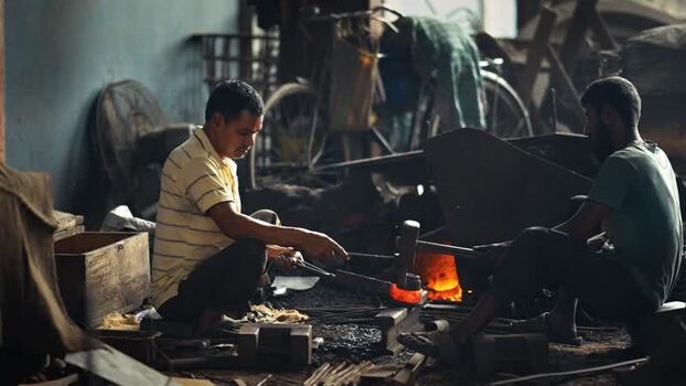View of blacksmiths forging glowing hot metal in a workshop Bangladesh.
