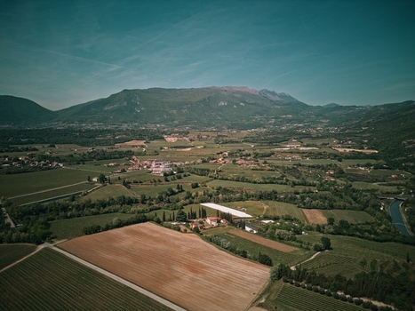 Aerial view of lush green vineyards cultivated fields and a small village nestled at the foot of rolling mountains under a clear blue sky Italy.