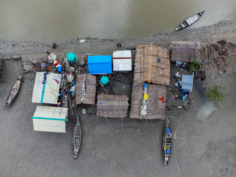 Aerial view of Kalabagi village featuring traditional thatched huts and wooden boats along the muddy riverbank in Khulna District Khulna Division Bangladesh.