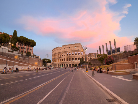 View of the Colosseum at sunset with a vibrant pink sky historic stone arches and people walking along the street in Roma Lazio Italy.