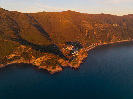 Aerial view of the historic village of Corniglia perched on a rocky cliff overlooking the Mediterranean Sea during golden hour with lush green mountains in the background Corniglia Liguria Italy. Aerial view of the historic village of Corniglia perched on a rocky cliff overlooking the Mediterranean Sea during golden hour with lush green mountains in the background Corniglia Liguria Italy.