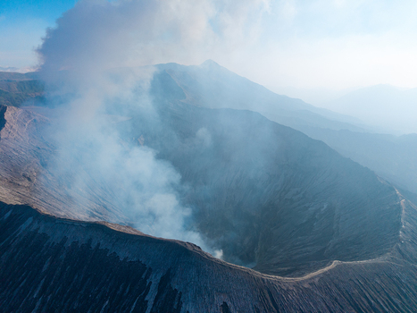 Aerial view of Mount Bromo crater with volcanic smoke rising from the caldera rugged terrain and hazy mountain landscape in Tosari East Java Indonesia.