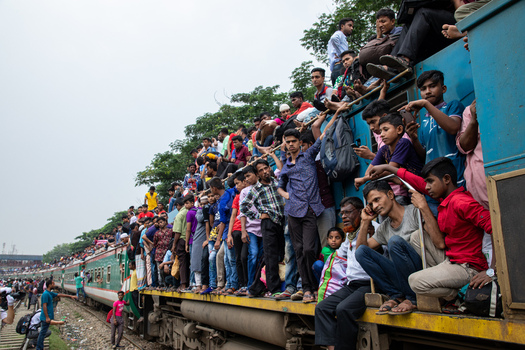 Dhaka Bangladesh 15 June 2018 View of crowds of passengers sitting on the roof and hanging from the sides of a moving train at Airport Railway Station under an overcast sky. Dhaka Bangladesh 15 June 2018 View of crowds of passengers sitting on the roof and hanging from the sides of a moving train at Airport Railway Station under an overcast sky.