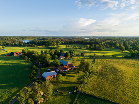 Aerial view of traditional red wooden farmhouses nestled among lush green meadows and dense forests under a soft blue sky Gundrastorp Skane County Sweden. Aerial view of traditional red wooden farmhouses nestled among lush green meadows and dense forests under a soft blue sky Gundrastorp Skane County Sweden.