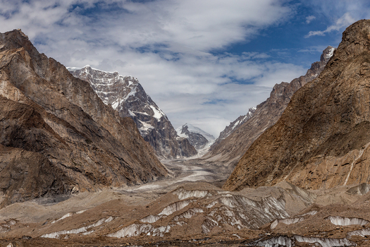 View of Baltoro Glacier surrounded by towering rugged snow capped mountain peaks under a cloudy sky in Baltoro Gilgit Baltistan Pakistan.