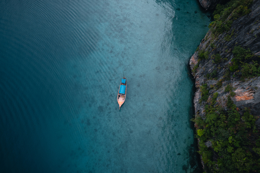Aerial view of a traditional long tail boat floating in the clear turquoise waters of Pi Leh Bay surrounded by dramatic limestone cliffs in Tambon Ao Nang Chang Wat Krabi Thailand. Aerial view of a traditional long tail boat floating in the clear turquoise waters of Pi Leh Bay surrounded by dramatic limestone cliffs in Tambon Ao Nang Chang Wat Krabi Thailand.