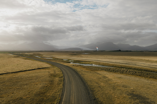 Aerial view of a kiteboarder on a small stream next to a dirt road in the vast landscape near the mountains of Hofn Sveitarfelagid Hornafjordur Iceland.