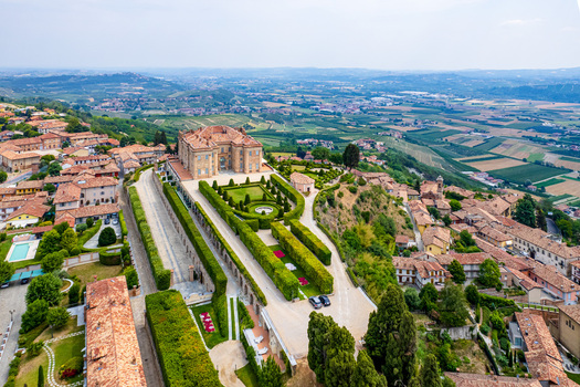 Aerial view of the historic Castello di Guarene with its elegant manicured gardens and the surrounding village rooftops overlooking the rolling hills of the Langhe region in Guarene Piedmont Italy. Aerial view of the historic Castello di Guarene with its elegant manicured gardens and the surrounding village rooftops overlooking the rolling hills of the Langhe region in Guarene Piedmont Italy.