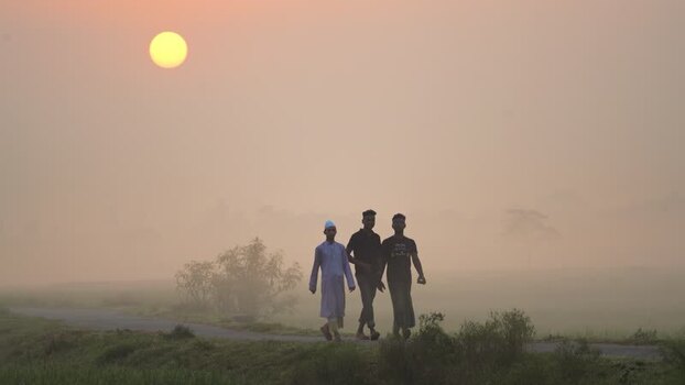 View of three men walking on a misty road at sunrise Bangladesh.