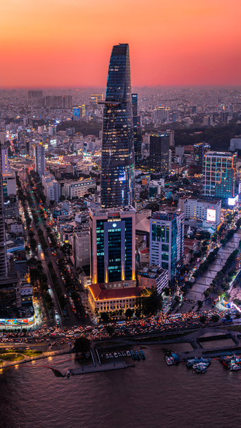 Aerial view of Bitexco Financial Tower rising above the urban skyline of Ho Chi Minh City at sunset with illuminated streets and the Saigon River. Ho Chi Minh City Vietnam. Aerial view of Bitexco Financial Tower rising above the urban skyline of Ho Chi Minh City at sunset with illuminated streets and the Saigon River. Ho Chi Minh City Vietnam.